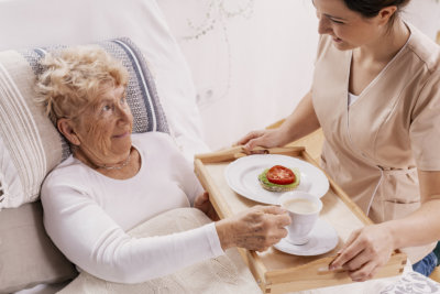 female elder receiving meals on bed from caregiver